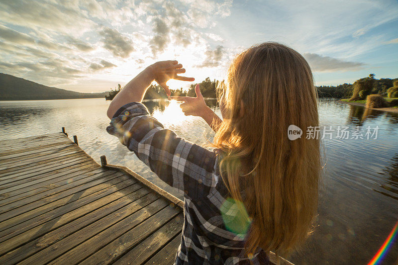 站在湖边码头上的女孩用手指勾勒夕阳