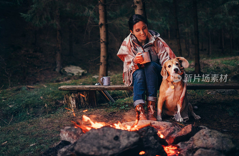 在森林里，女人和狗在篝火旁取暖