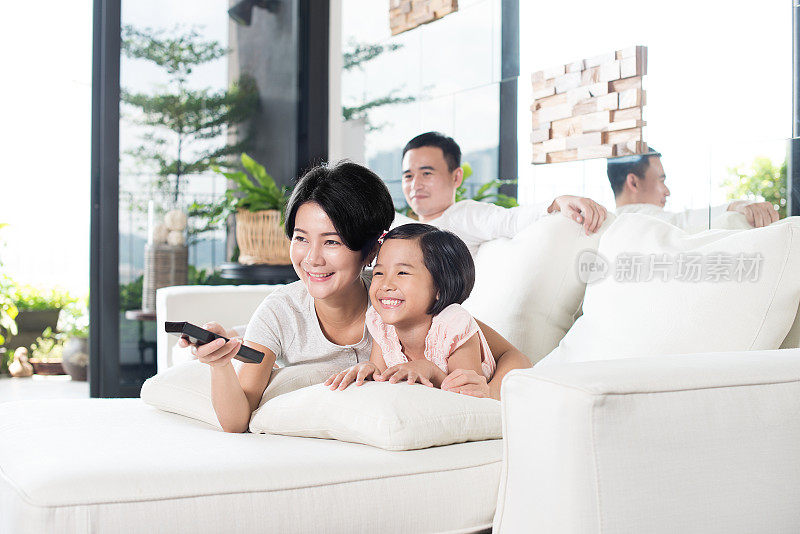 年轻的亚洲家庭在家里看电视。