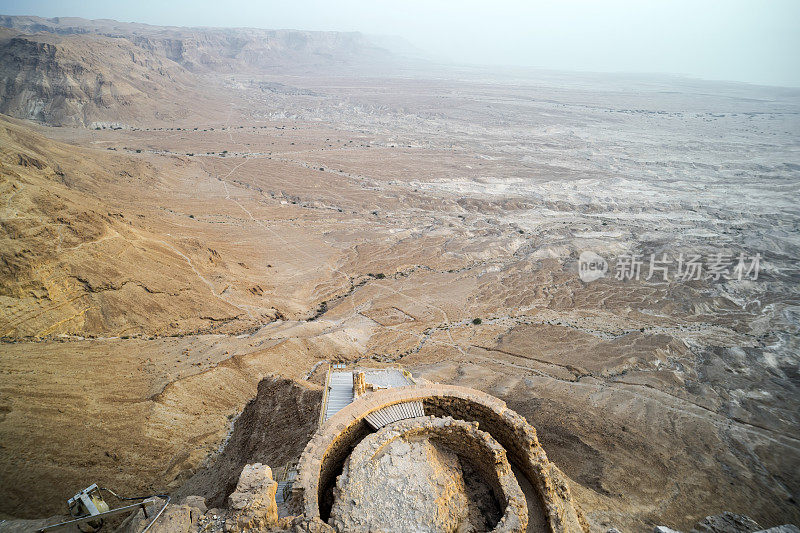 鸟瞰图的希律王堡垒废墟对山谷丘陵在犹大沙漠，以色列。死海海岸附近的高地上有古代人类建筑的遗迹。马察达堡