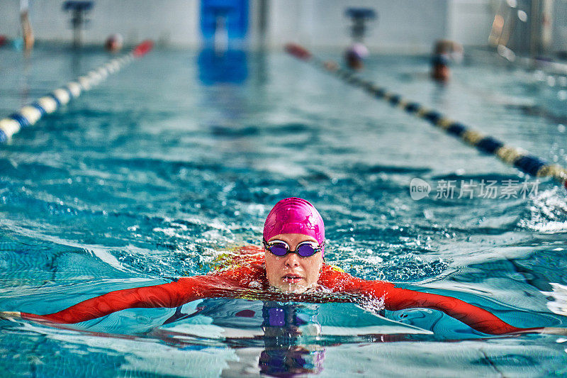 女运动员穿着红黄相间的泳衣在游蛙泳。水花四溅向不同的方向。