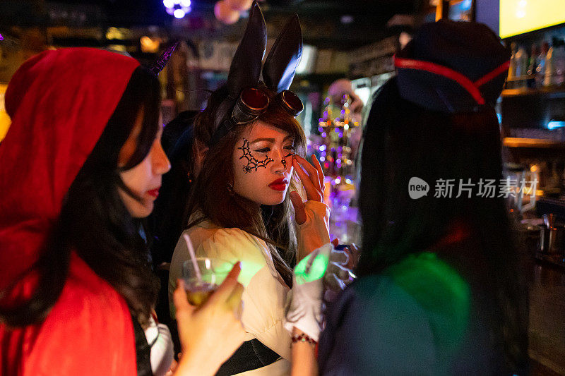 穿着万圣节服装的亚洲女人在夜店边聊天边喝鸡尾酒
