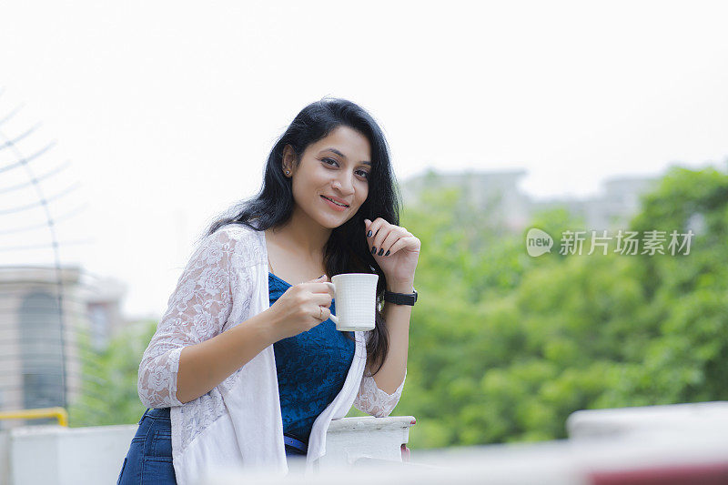 女人放松在阳台上拿着一杯咖啡或茶库存照片