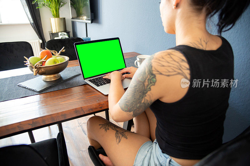年轻女子在家里用笔记本电脑工作-绿色屏幕的拷贝空间