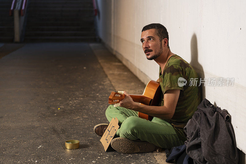 无家可归的街头艺人正在城市地下弹奏吉他，等待捐赠