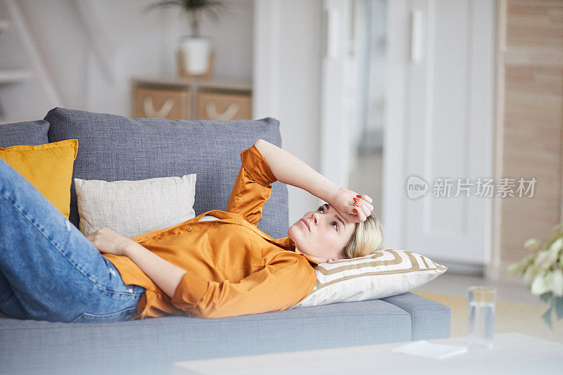 悲伤的年轻女子在橙色衬衫躺在心理分析师的沙发上，手在额头上，而看着天花板