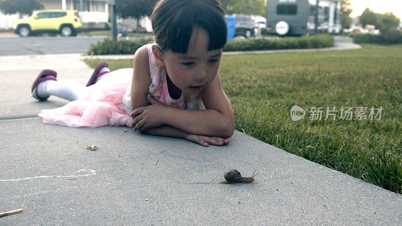 4岁的小女孩和年轻的母亲在观察一个花园蜗牛在他们的前车道在一个中产阶级的社区