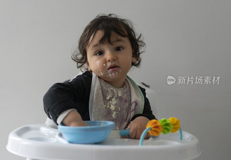 可爱的小男孩在一团乱麻中学习自食其力，坐在高高的椅子上