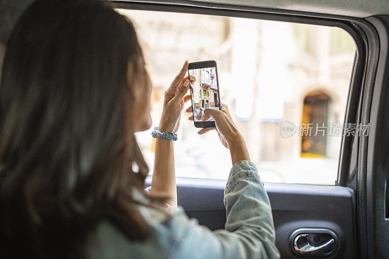 年轻女性游客在出租车上用智能手机拍照