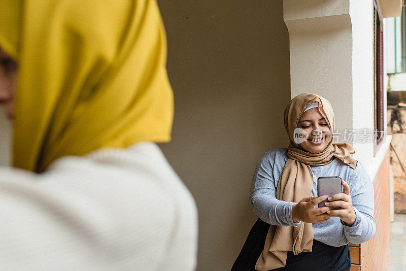 微笑的穆斯林妇女在阳台上使用智能手机
