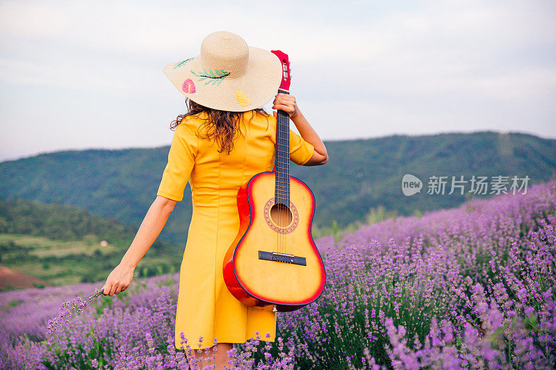 一个拿着吉他的女人走过盛开的薰衣草田
