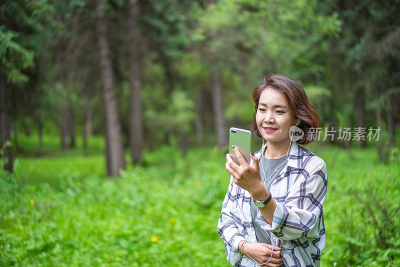 年轻的亚洲女子在森林里戴着耳机听音乐