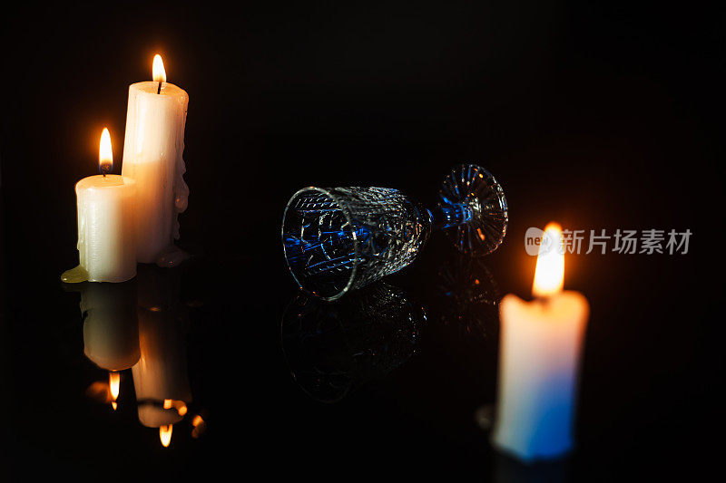 翻倒的水晶玻璃放在蜡烛之间的暗色镜子桌上，侧面。盛宴或庆典概念
