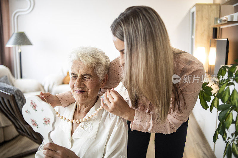 孙女给她的祖母戴上了一条漂亮的项链——一个漂亮的年轻女人在和她的祖母说话——祖母和孙女照镜子