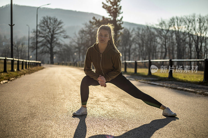 一个年轻的健康女孩谁训练在一个温暖的冬天的一天在户外-一个年轻迷人的健身女人在运动服锻炼在外面清晨
