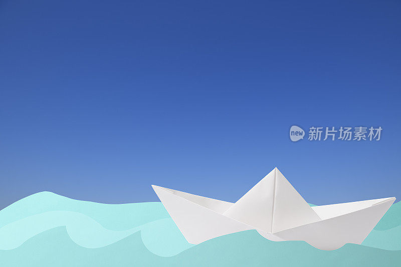 空白的折纸船漂浮在蓝色的纸波在晴朗的天空