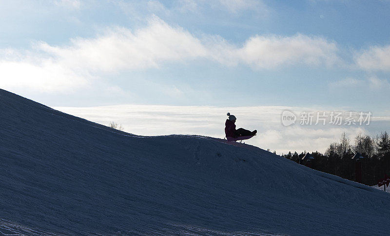 一位年轻的女子乘着雪橇快速滑下一座积雪覆盖的山。太阳背景下一个年轻女子的剪影。