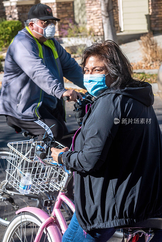 一个成熟的女人骑着自行车，戴着防护口罩看着摄像机