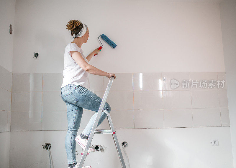 一个穿着白色t恤的女人站在梯子上粉刷墙壁的侧面