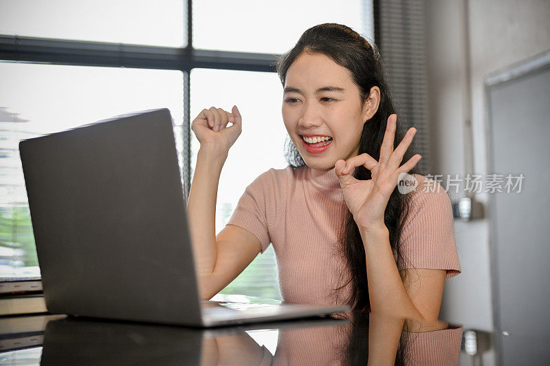 快乐的亚洲女性使用笔记本电脑与她的朋友视频通话，做一个Okay的手势