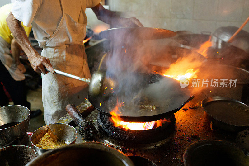 亚洲厨师在锅里翻炒。戏剧性的烹饪与炉子的火