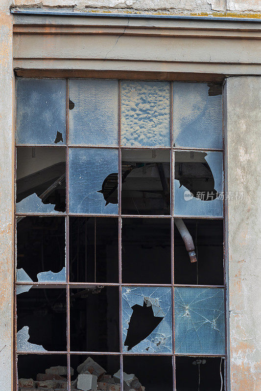一座老建筑的窗户。窗户上有一个金属结构。玻璃碎了。墙在剥落。