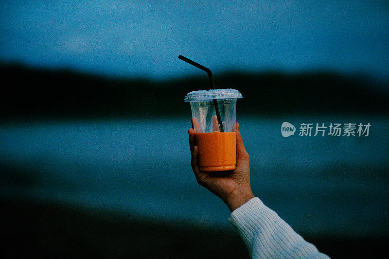 女人的手拿着棕榈杯泰国奶茶与海滩背景。