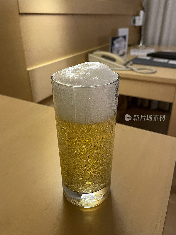 高玻璃品脱啤酒的特写图像，显示气泡和泡沫头，酒店床头柜，客房服务茶点，重点在前景