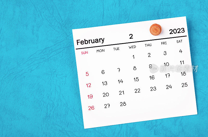 2023年2月的月历和蓝色背景的木制图钉。