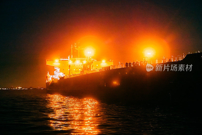 在加利福尼亚州亨廷顿海滩附近的太平洋上，夜晚，一艘大型货船上明亮的灯光在雾中闪烁