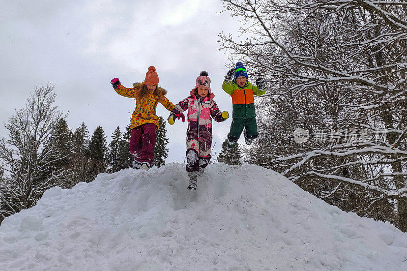 三个孩子是白种人，兴高采烈地从一堆雪上跳下来。