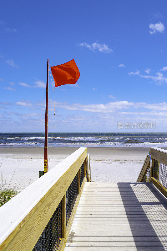 红旗在海滩入口甲板上迎风飘扬，JAX上的危险海滩状况警告在阳光明媚的暴风雨中，佛罗里达州杰克逊维尔