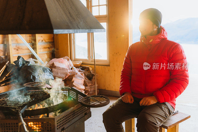 挪威峡湾，一名男子在炉火旁取暖