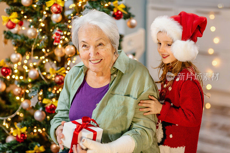 亲戚们在平安夜给奶奶送礼物。快乐的家庭成员坐在装饰好的圣诞树旁