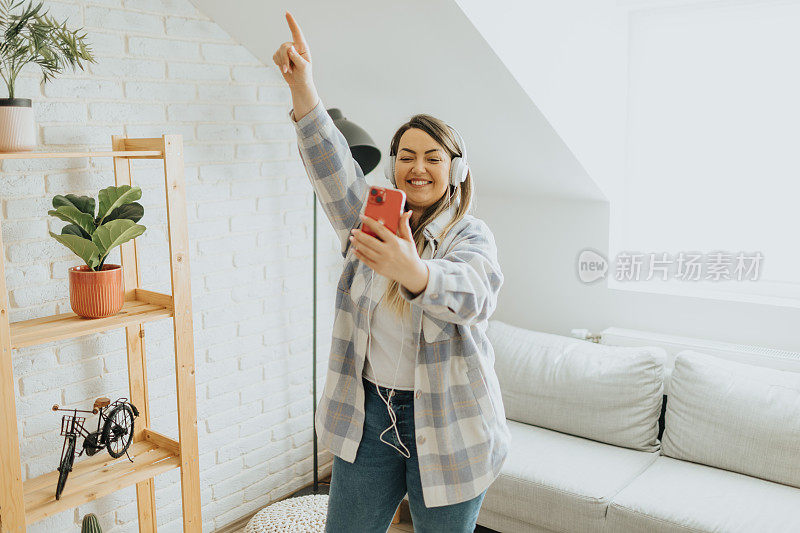 开朗的年轻女子一边在家里戴着耳机一边唱歌跳舞