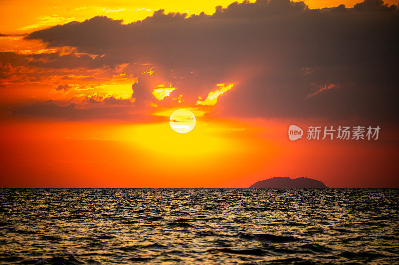 海洋上火热的日落，充满活力的橙色和红色阴影描绘着天空。太阳戏剧性地落下，在黑暗的水面上投下温暖的光芒，创造出令人惊叹的自然画布反射