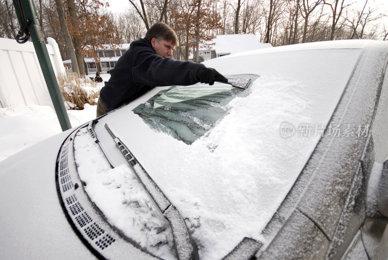 一个男人在刮挡风玻璃上的冰雪