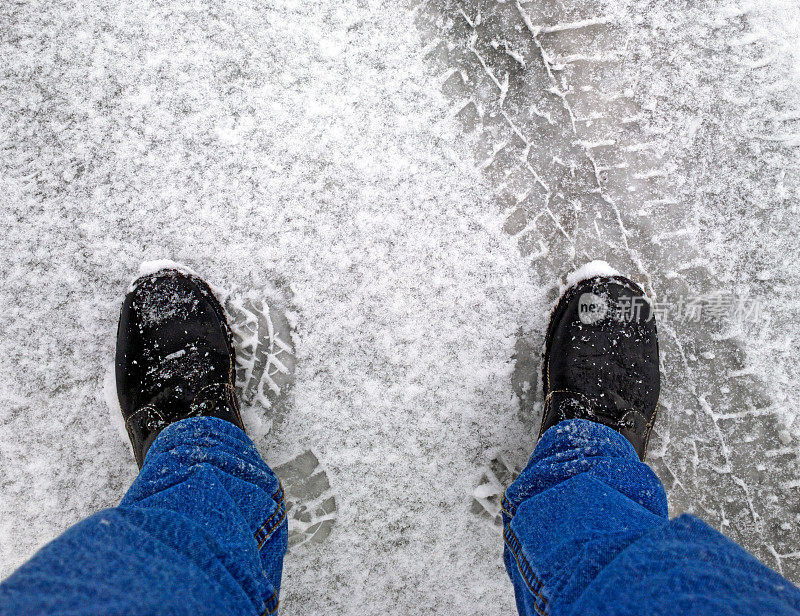 脚踩在雪地里的柏油路上。