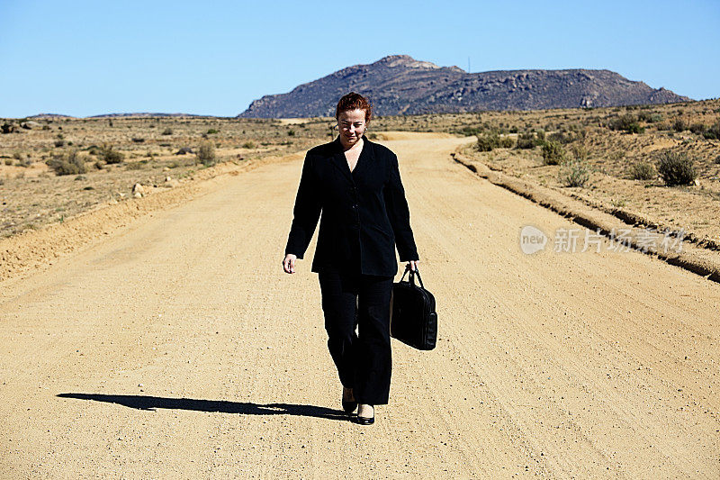 一个穿着西装的女人走在一条偏僻的土路上