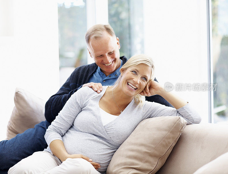 微笑的孕妇与她的丈夫在沙发上放松
