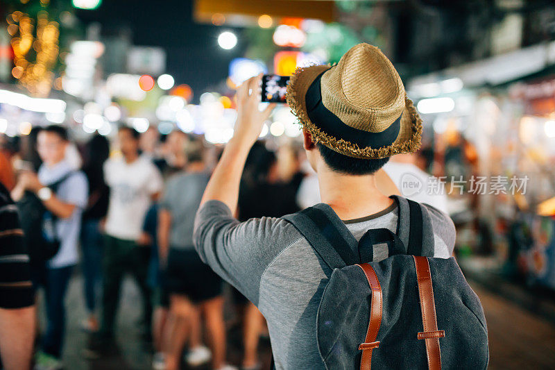年轻的亚洲旅行者在夜晚的街道上用手机拍照
