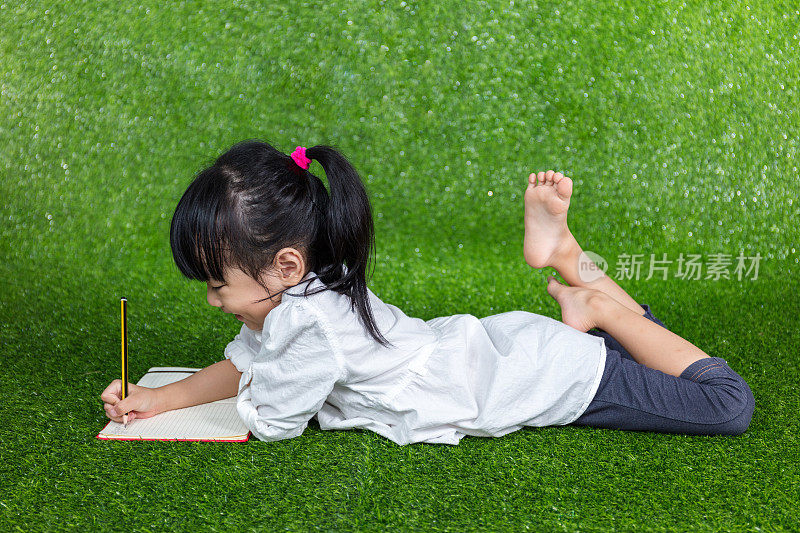 亚洲华人小女孩躺在草地上写字