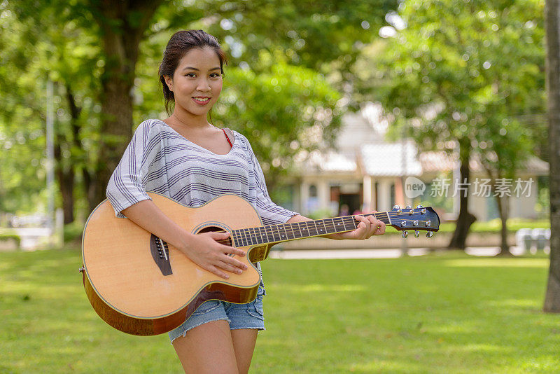 年轻美丽的亚洲女人的肖像与吉他放松在公园的户外