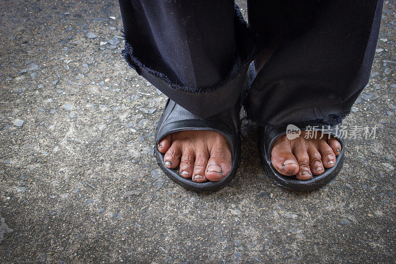 一个男人的脏脚站在旧的水泥地板上。