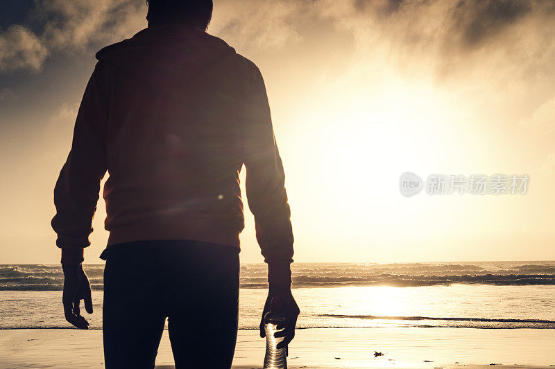 一名男子沿着海滩跑步后，站在日落时分的海滩上。