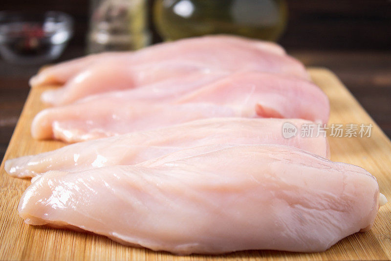 在木桌的背景下，一块切菜板上放着生鸡肉片。烹饪用的肉类配料。