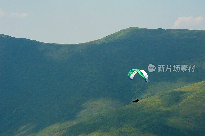 在一个阳光明媚的夏日，滑翔伞飞过山谷。