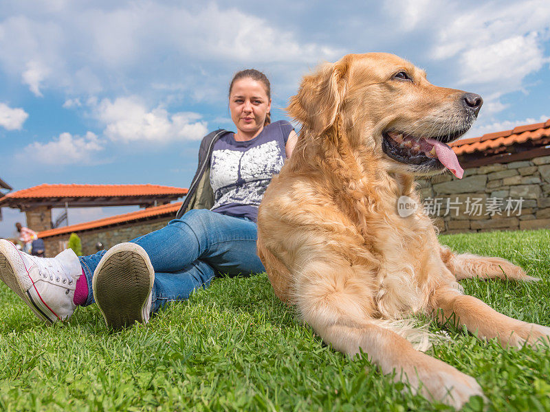 女孩和她的金毛猎犬坐在外面的草地上