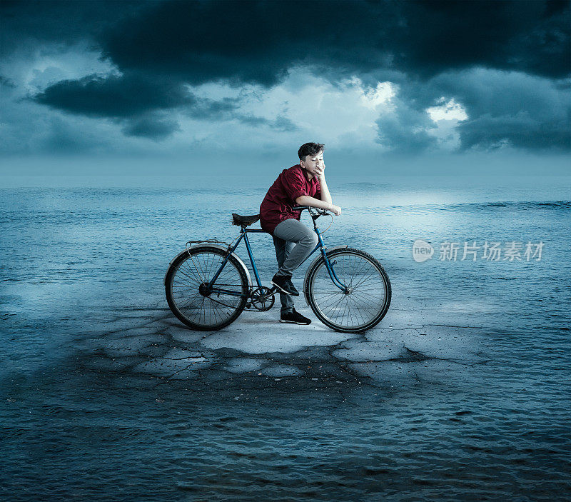 一个年轻人骑着自行车站在大海中央的一段路上。