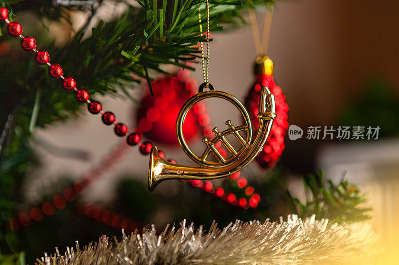 一个金色的法国圆号圣诞装饰品在人造圣诞树上的特写-聚焦在圆号上